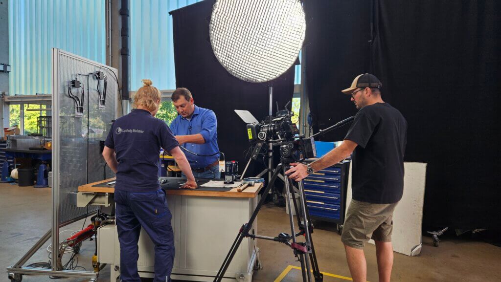 Videoproduktion bei Ludwig Meister für Staffel 12. Ein Experte erklärt technische Abläufe an einer Werkbank, während Kamera- und Lichtteam die Schulungsvideos professionell aufnehmen.