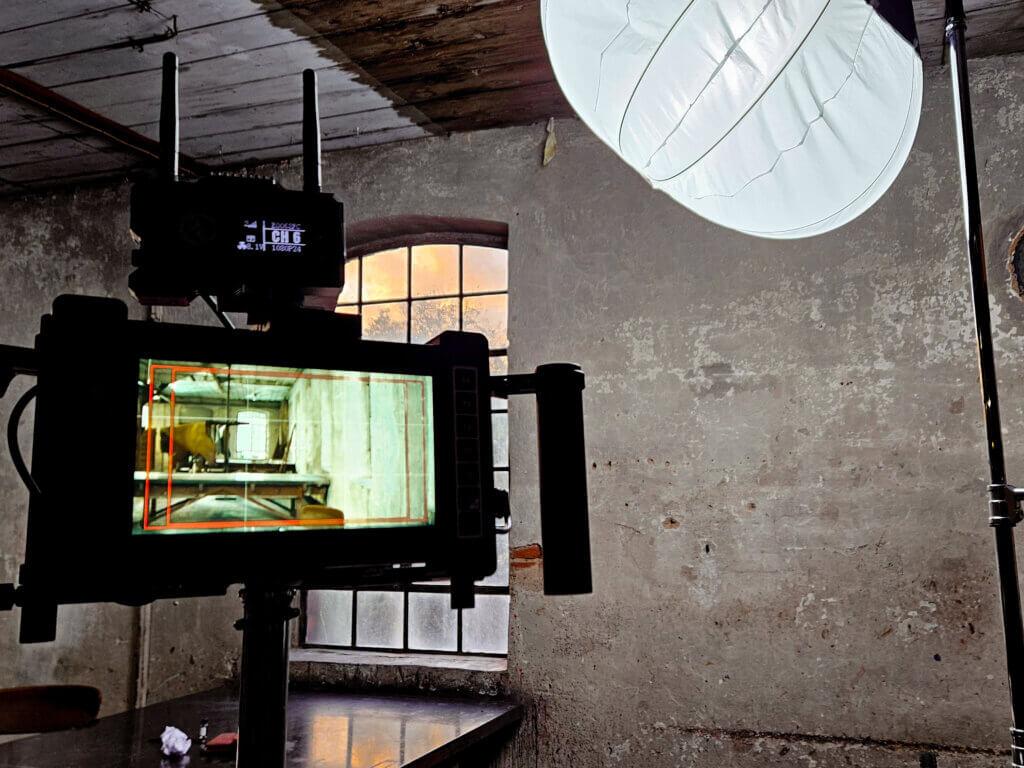 Monitor zeigt die Kameravorschau eines Musikvideodrehs in einer alten Industriehalle, daneben ein großes Softlight und die raue Backsteinwand des Röhm in Schorndorf.